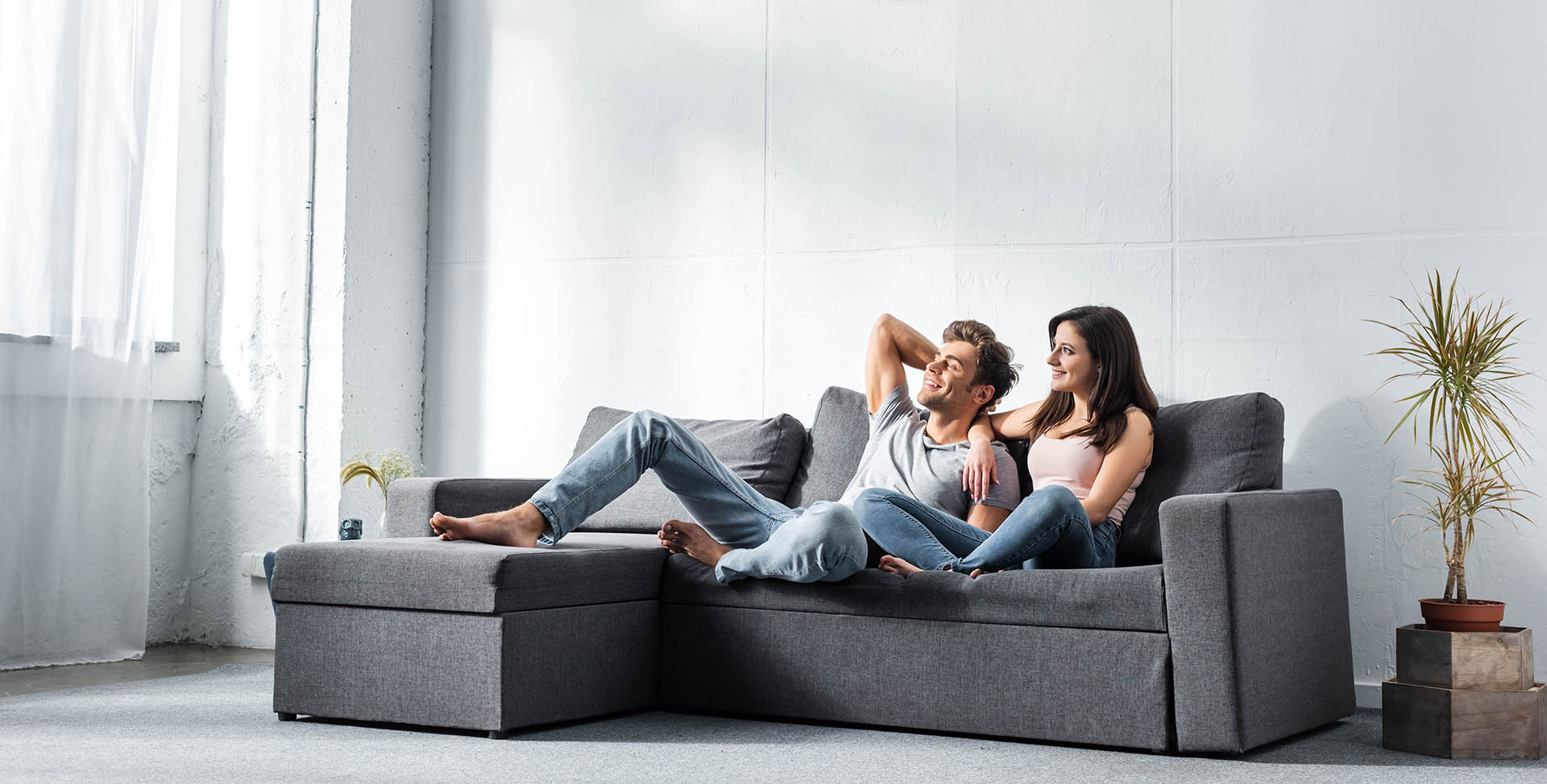 Man and a woman relaxing on a gray sectional sofa in a modern living room.